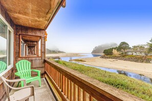 A wooden balcony with two green Adirondack chairs, overlooking a beach and a river. - Oceanfront 2nd floor condo with river ocean views balcony (Neskowin)