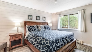 A bedroom with a bed, nightstand, and window. - Oceanfront 2nd floor condo with river ocean views balcony (Neskowin)