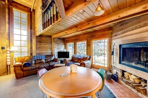 Un intérieur de chalet chaleureux, avec un revêtement en bois, une cheminée, un téléviseur et un coin repas.