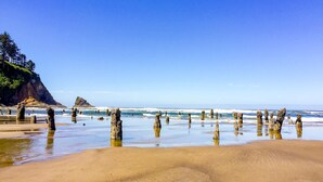 Una playa con formaciones rocosas en el agua y un acantilado boscoso al fondo.