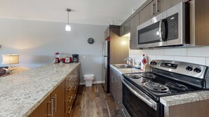 Una cocina con encimera de granito, electrodomésticos de acero inoxidable, armarios de madera y un reloj en la pared.