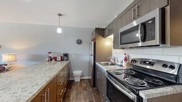 A kitchen with a granite countertop, stainless steel appliances, wooden cabinets, and a clock on the wall.