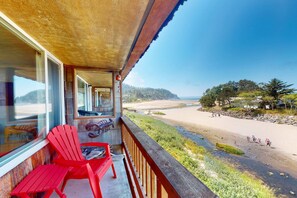 A balcony with red chairs and a view of a beach. - Third floor beachfront condo with a balcony full kitchen and ocean views (Neskowin)