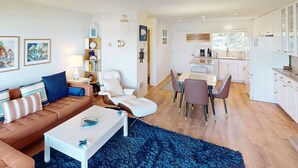 Uma sala de estar moderna com um sofá marrom, uma mesa de centro branca e um espaço de jantar com mesa e cadeiras.