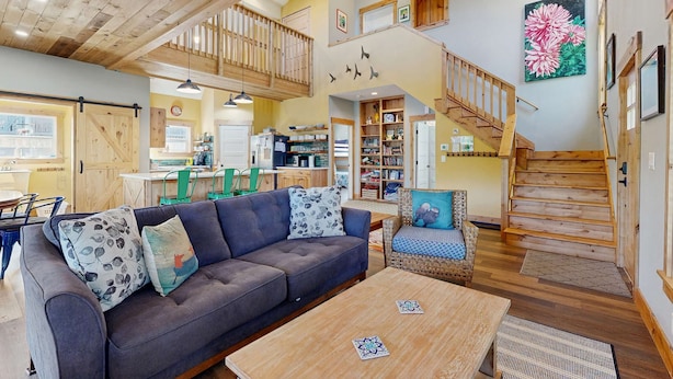 A spacious living area with a wooden staircase, a sofa with patterned cushions, and a dining table. - Newly constructed home with firepit and large deck walk to the beach and golf (Neskowin)