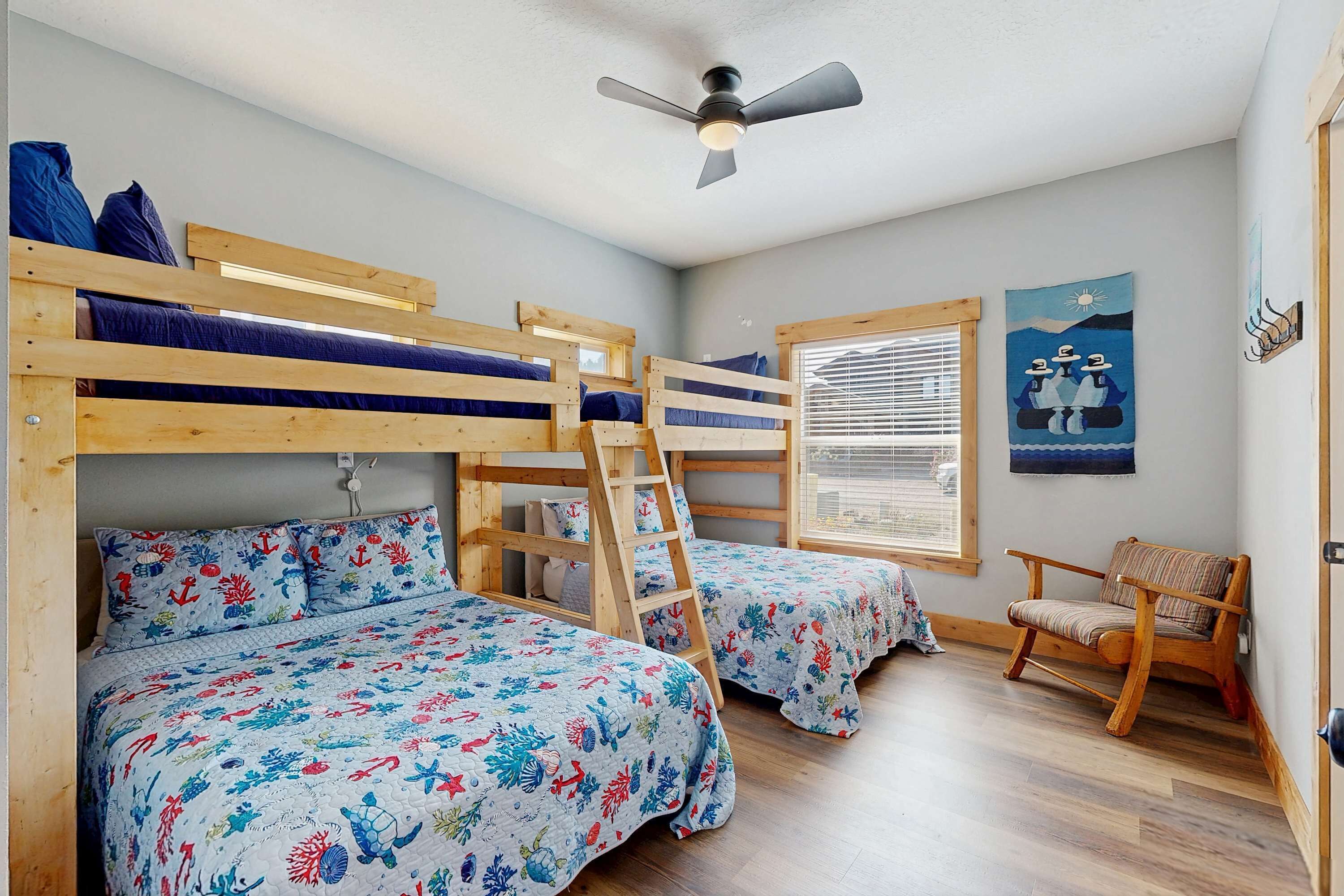A room with bunk beds, a ceiling fan, a window with blinds, and a chair.