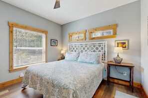 Quarto com uma cama grande, cabeceira de madeira, duas mesas de cabeceira com luminárias e uma janela com persianas.