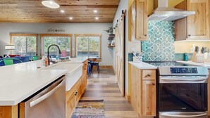 A modern kitchen with wooden cabinets, a stainless steel dishwasher, a built-in oven, and a patterned backsplash. - Newly constructed home with firepit and large deck walk to the beach and golf (Neskowin)