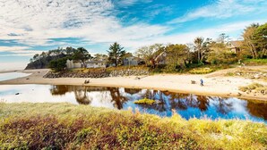 A coastal landscape with a beach, a small pond, and houses in the background. - Creekside condo with beach access balcony full kitchen and ocean views (Neskowin)