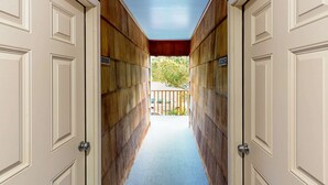 A corridor with wooden walls and white doors, leading to a balcony with a view of greenery. - Creekside condo with beach access balcony full kitchen and ocean views (Neskowin)