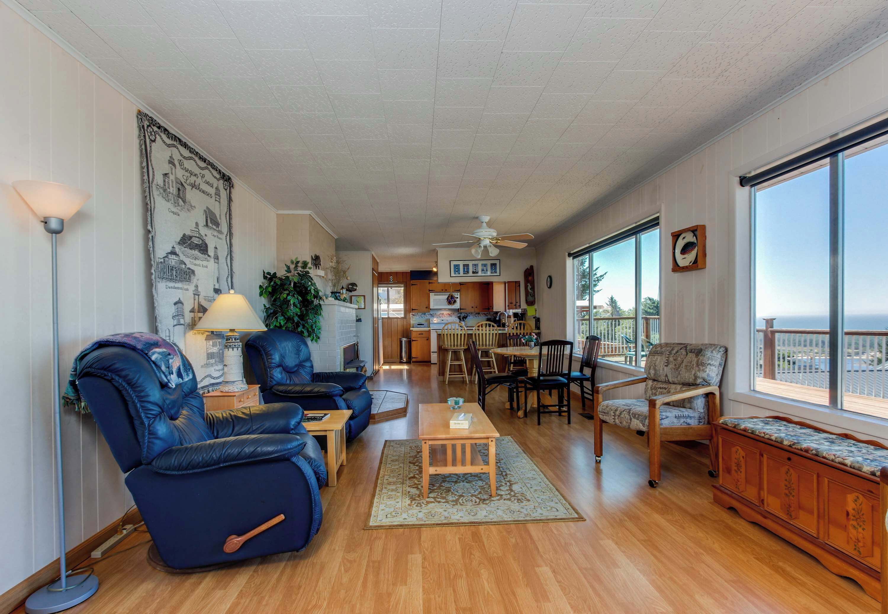 A spacious living room with a blue recliner, a wooden coffee table, and a view of the kitchen and balcony.