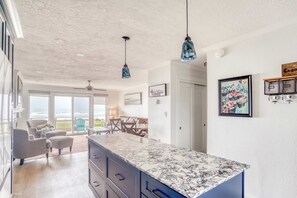 A modern kitchen with a marble countertop, pendant lights, and a view to the outside. - Renovated Oceanfront Condo w/Beach Access & Views | Pet-Friendly (Neskowin)
