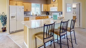 Una cocina con armarios de madera, un refrigerador, un microondas y una isla grande con taburetes de bar.