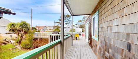 A wooden deck with a green railing, a covered porch, and a view of the neighborhood.