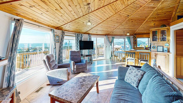 A spacious living area with a wooden ceiling, a sofa, armchairs, a coffee table, and a TV. - Spacious Dog Friendly Getaway with Boat Parking Perfect for Two Families (Pacific City)