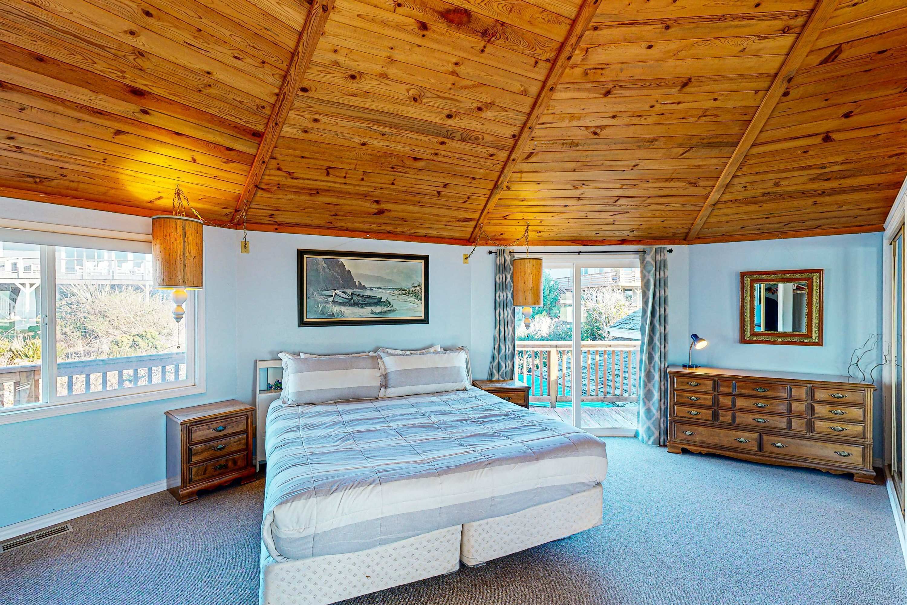 Une chambre avec un plafond en bois, un grand lit, une commode et un tableau accroché au mur.