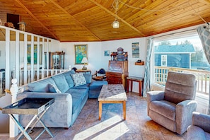 Un salon chaleureux avec un plafond en bois, un canapé, un fauteuil inclinable, une table basse et une fenêtre donnant sur l’extérieur.