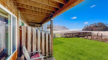 A wooden building with a balcony overlooking a beach and a grassy area.