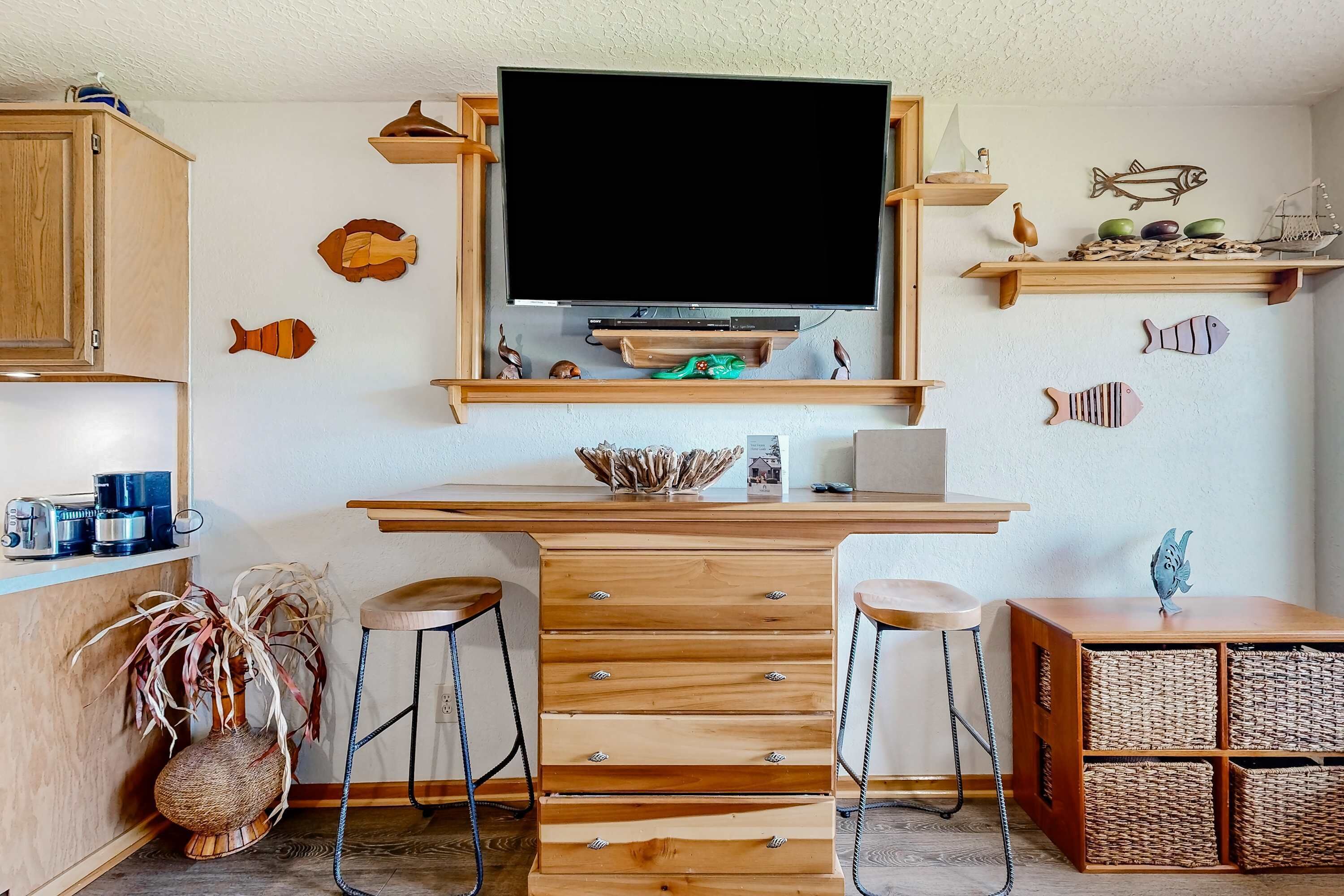 Une cuisine compacte dotée d’un plan de travail en bois, de deux tabourets de bar, d’un téléviseur fixé au-dessus du plan de travail et d’une décoration murale représentant des poissons.