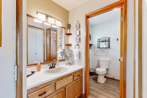 A bathroom with a wooden vanity, a sink, a mirror with lights, a toilet, and a shower area. - Beachfront dog friendly studio with amazing Proposal Rock view steps to the sand (Neskowin)