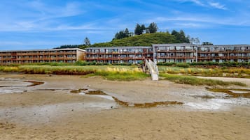 A multi-story building with a wooden facade and balconies, situated near a natural landscape with a clear sky.