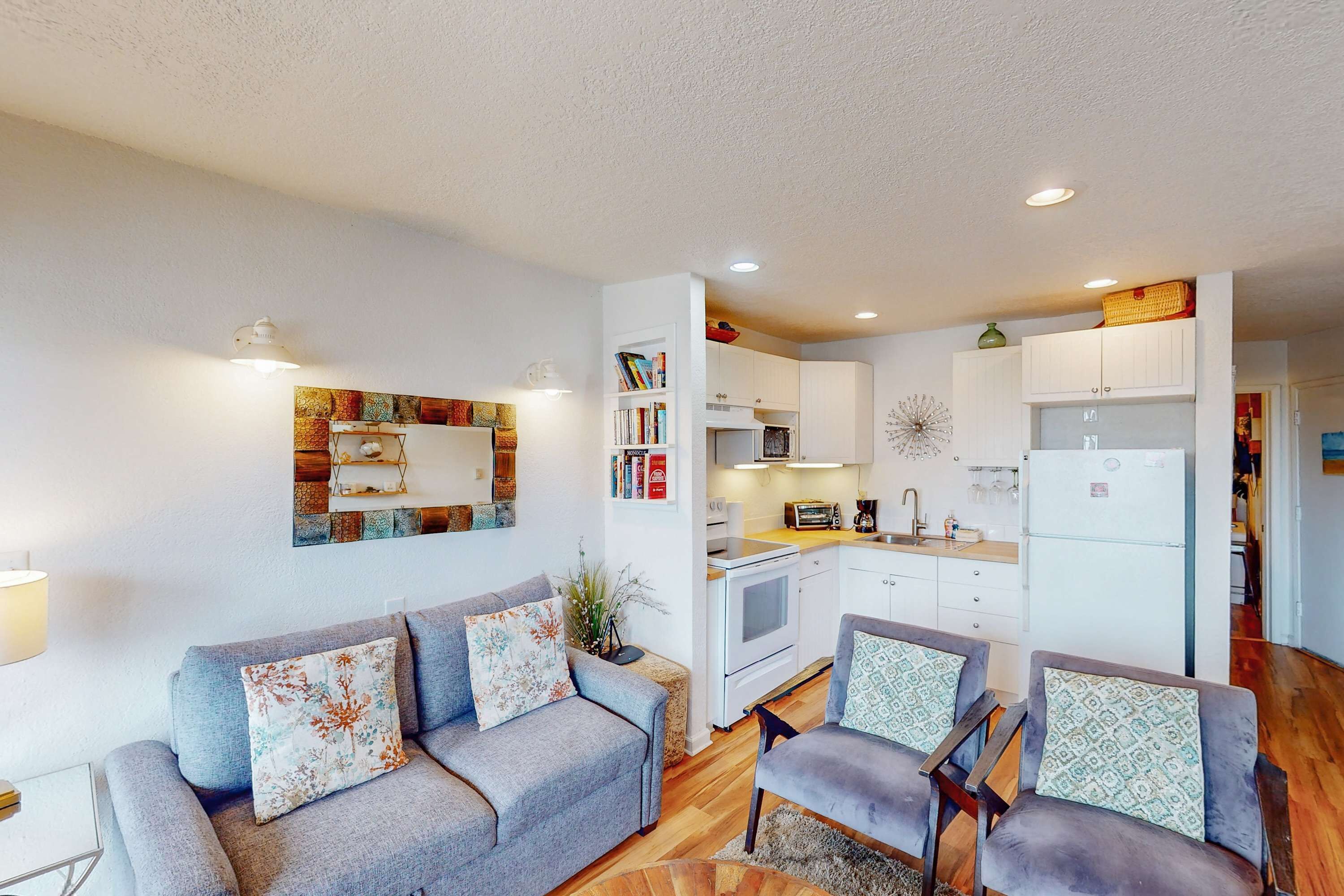 A compact living space with a grey sofa, two armchairs, a kitchenette, and a dining area.