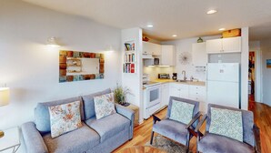A compact living space with a grey sofa, two armchairs, a kitchenette, and a dining area. - Oceanfront 2nd floor condo with ocean views balcony and seasonal beach access (Neskowin)