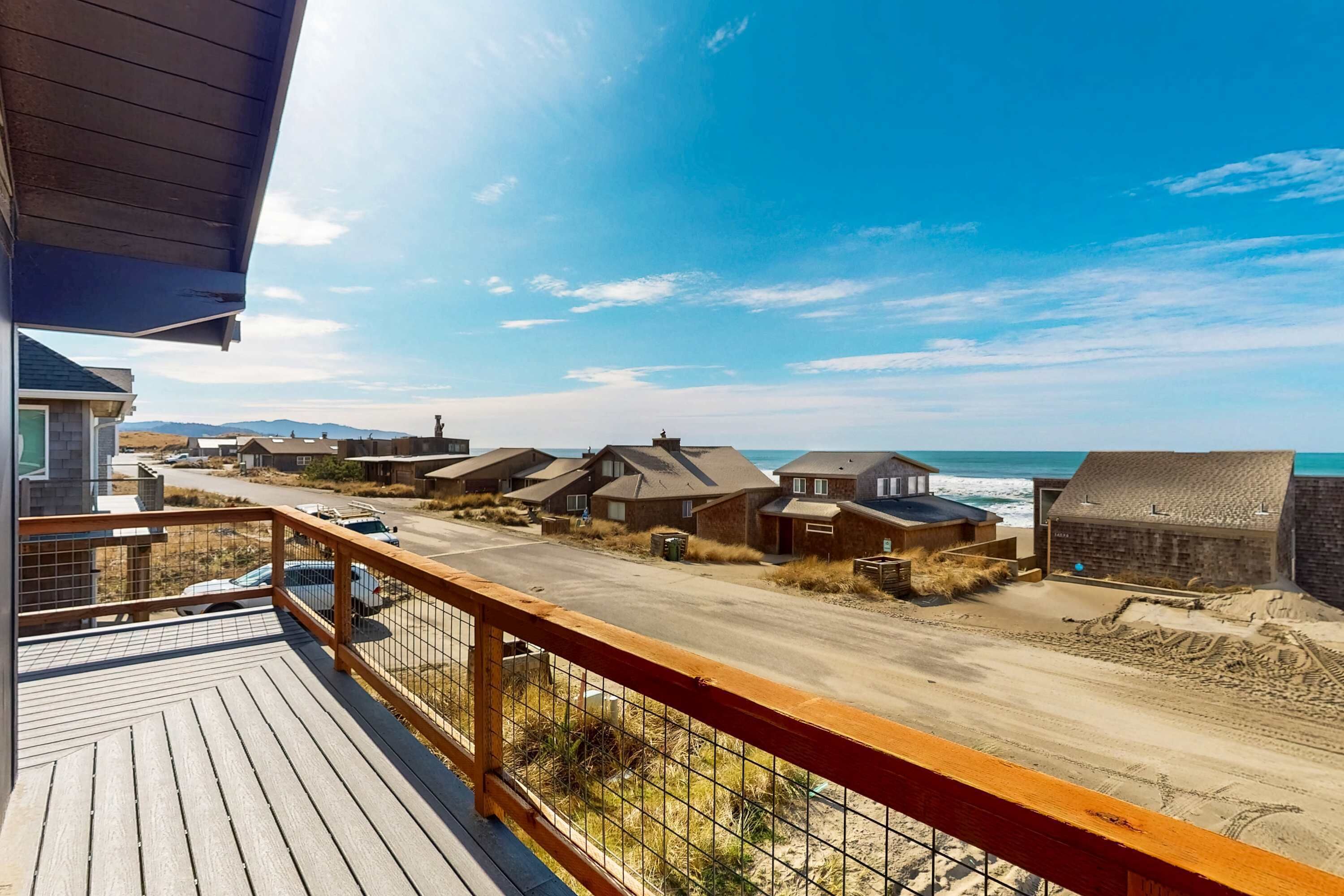 A wooden deck with a railing overlooking a beach with houses and a clear sky.