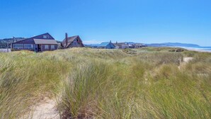 Ein Küstenhaus mit sandigem Vordergrund und freiem Blick auf den Strand und die fernen Hügel.
