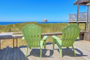 Deux chaises Adirondack vertes sont placées sur une terrasse en bois, d’où l’on a vue sur une plage et, au loin, sur une formation rocheuse.