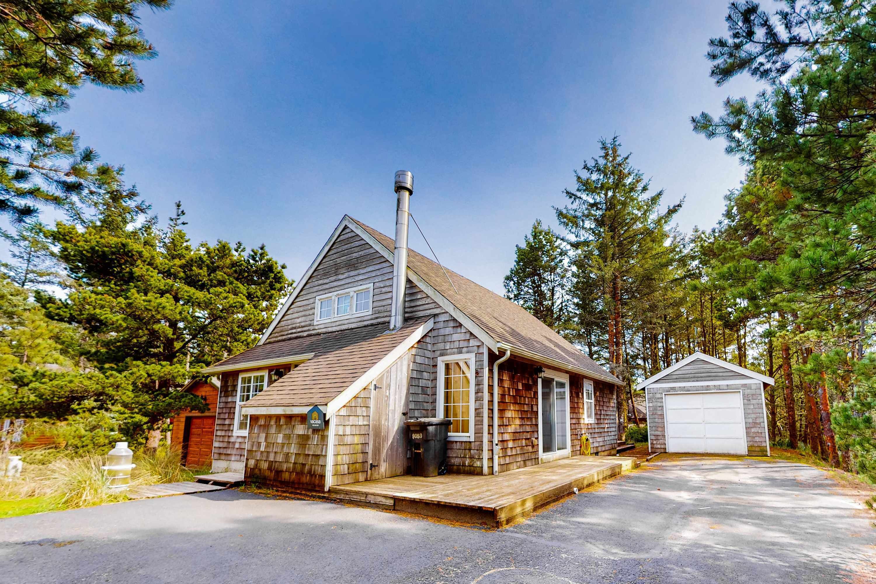 Une maison en bois à deux étages, dotée d’un garage et entourée d’arbres.
