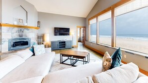 Ein großzügiges Wohnzimmer mit Kamin, einem großen Fenster mit Blick auf den Strand und einer gemütlichen Sitzecke.