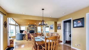 Un comedor amplio con una mesa y sillas de madera, un candelabro, y vistas al salón y la cocina de fondo.