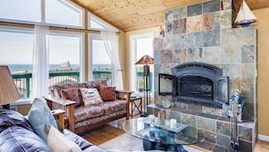 Un salón acogedor con chimenea de piedra, ventanas amplias y vista al mar.