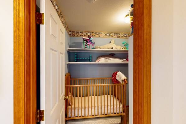 Una habitación pequeña y acogedora con una cuna de madera, un estante con juguetes y un borde decorativo.