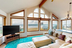 Amplia sala de estar con un televisor de pantalla plana grande, un sofá modular color beige y vista a la playa a través de amplias ventanas.