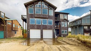A multi-story residential building with a garage, a balcony, and a covered porch area. - Gorgeous waterfront home with ocean views a furnished deck and beach access (Pacific City)