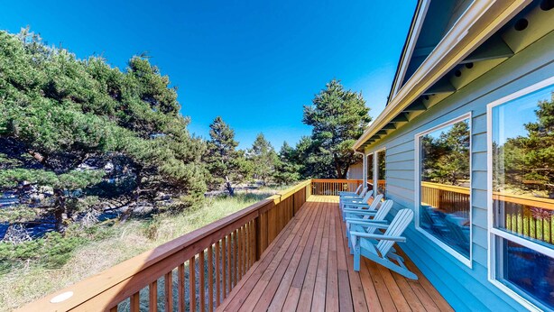A wooden deck with white chairs, overlooking a forested area. - Bright dog friendly home with wrap around deck just steps from beach (Pacific City)