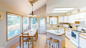 A spacious kitchen with wooden cabinets, a large island, and a view of the outdoors. - Bright dog friendly home with wrap around deck just steps from beach (Pacific City)