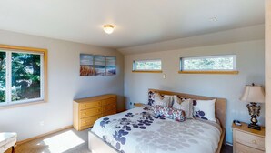 A bedroom with a bed, dresser, nightstand, lamp, and artwork on the walls. - Bright dog friendly home with wrap around deck just steps from beach (Pacific City)