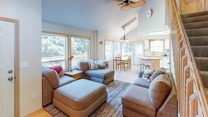 A spacious living area with a large window, a ceiling fan, and a staircase leading to an upper level. - Bright dog friendly home with wrap around deck just steps from beach (Pacific City)