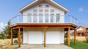 Uma casa de dois andares com varanda, duas garagens e um deck de madeira.