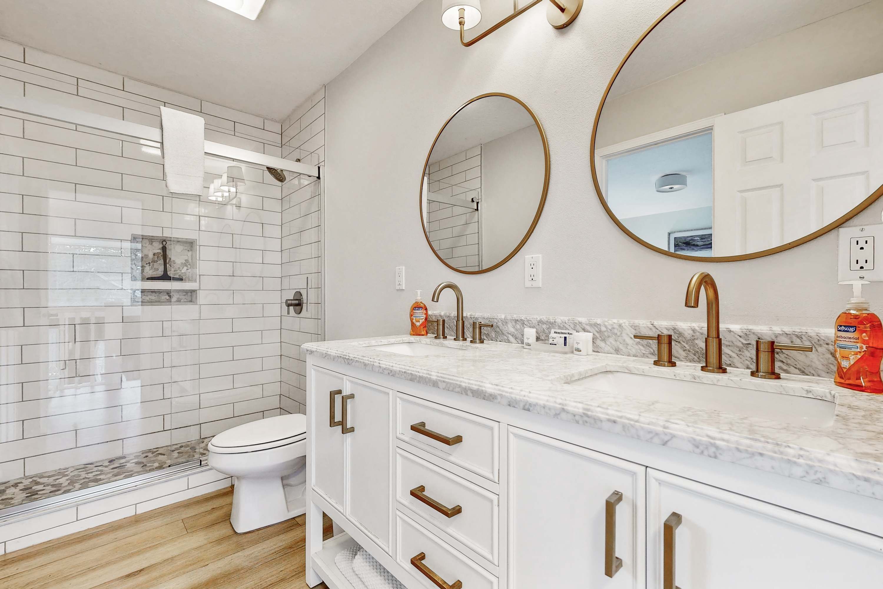 A modern bathroom with a white vanity, two gold faucets, and a large mirror.