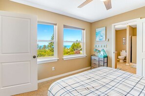 Ein Schlafzimmer mit einem Bett, zwei Fenstern, einem Deckenventilator und Blick ins Freie.