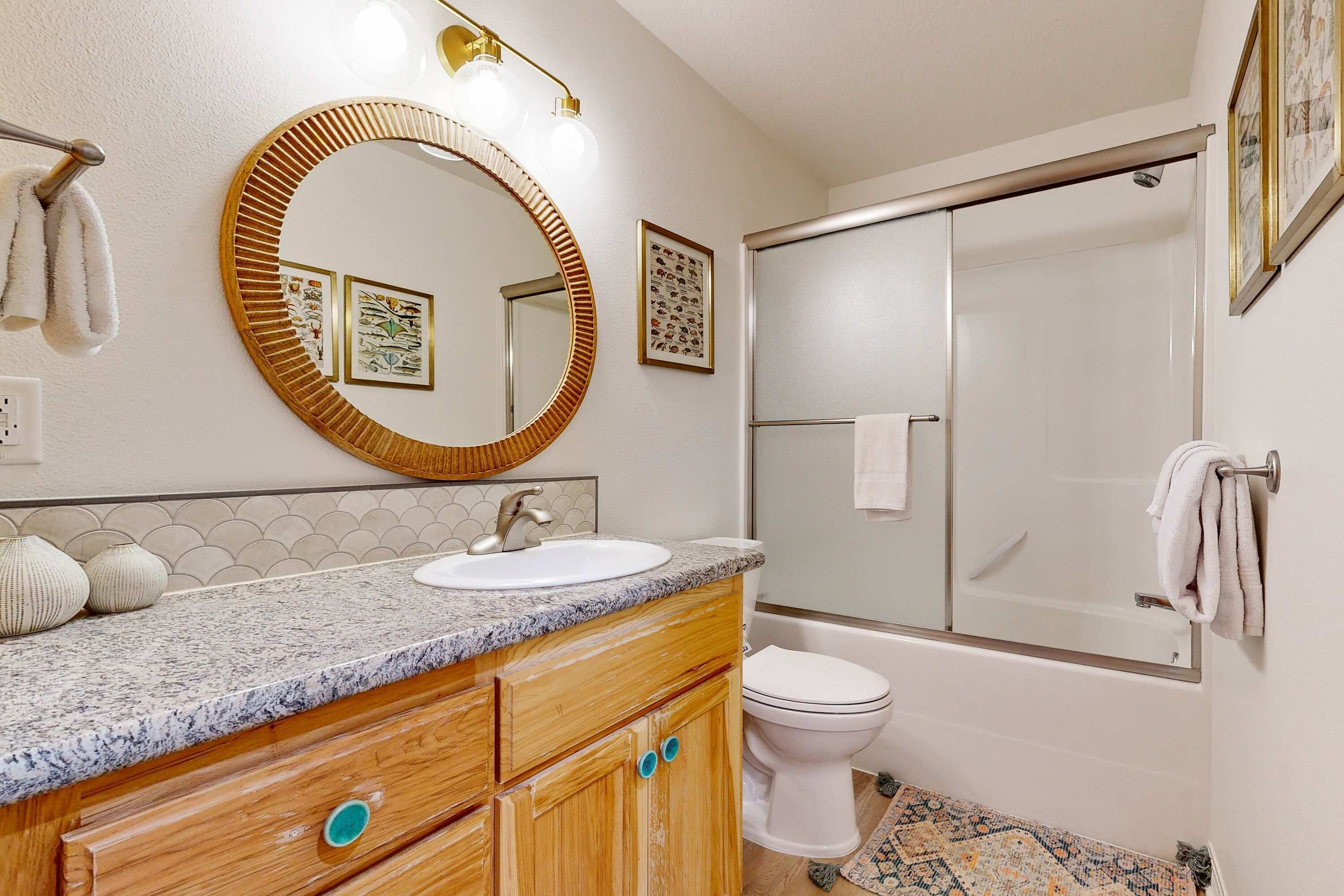 A bathroom with a round mirror, a sink, a toilet, and a shower.