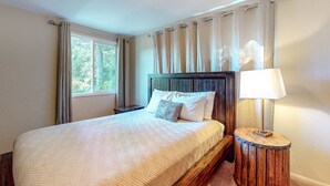 Un lit bien fait, avec une tête de lit en bois, une lampe de chevet et une fenêtre avec des rideaux.