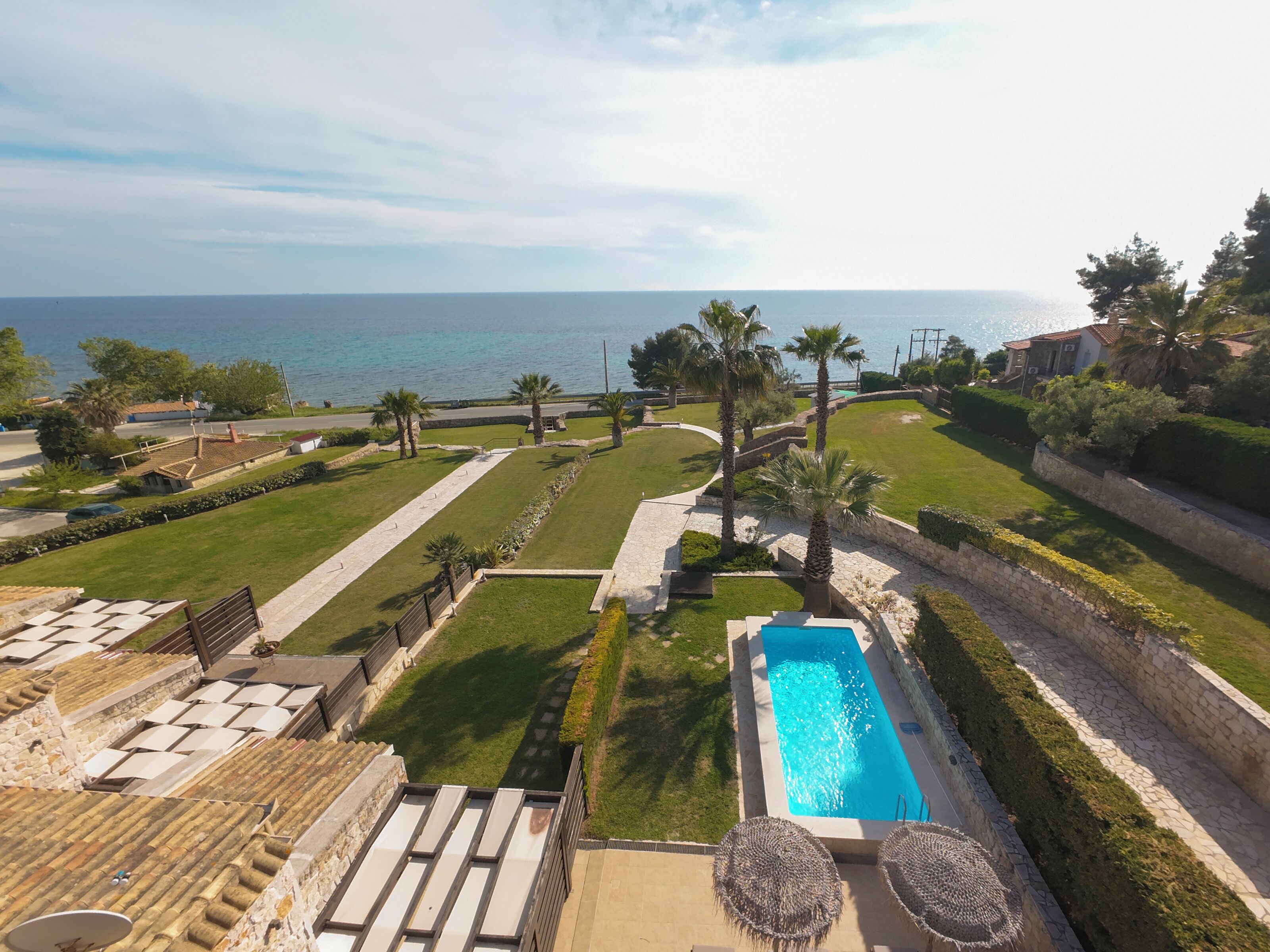 A rooftop pool with a view of the sea, surrounded by well-maintained lawns and palm trees.