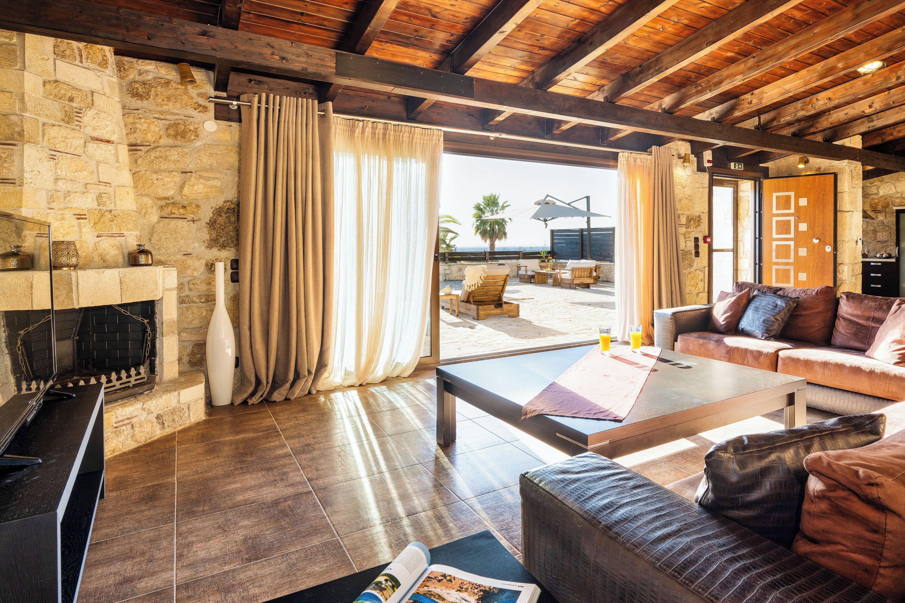 A spacious living area with a stone wall, wooden ceiling, and a view of the outdoors.