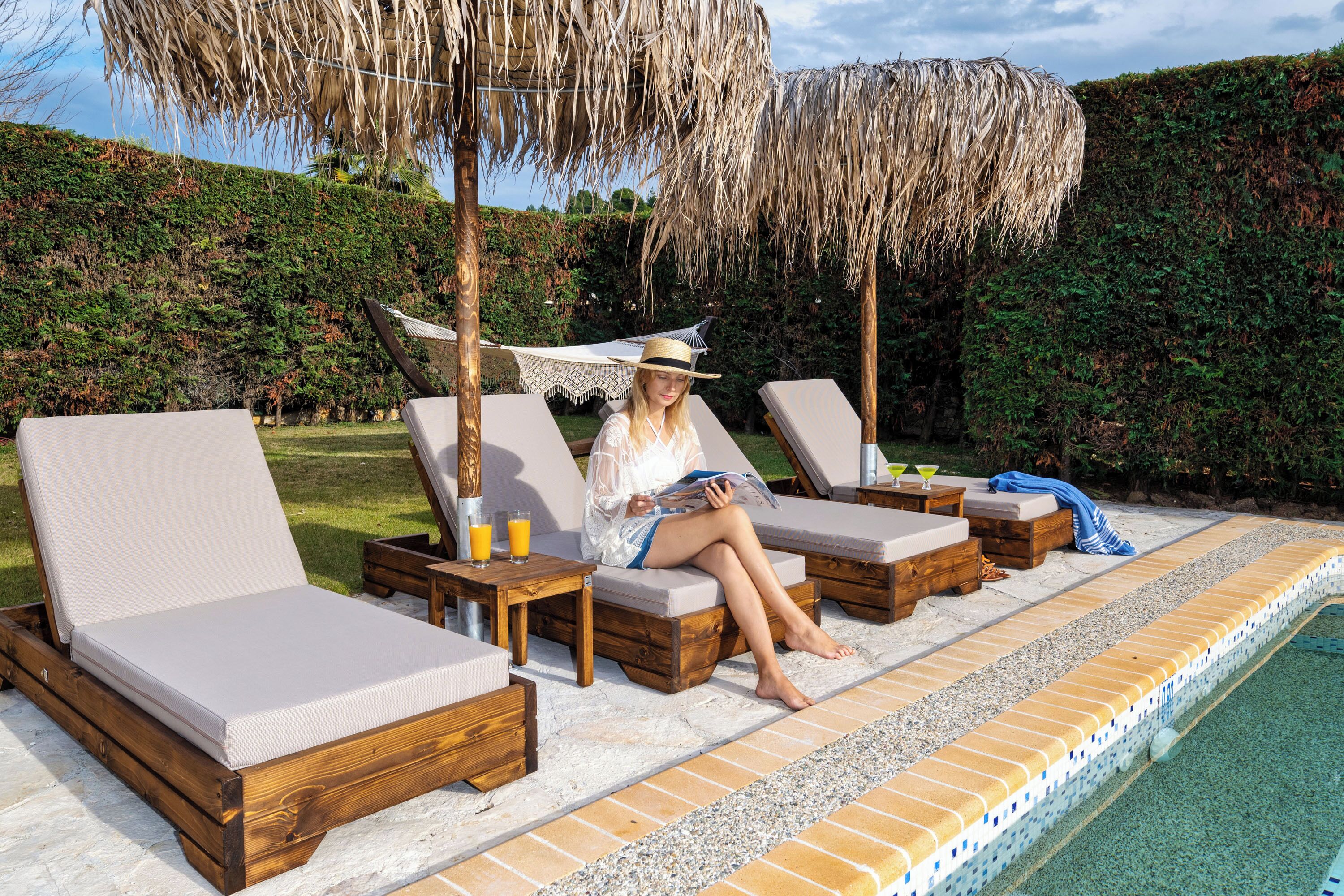 A poolside area with lounge chairs, a wooden table, and a thatched umbrella.