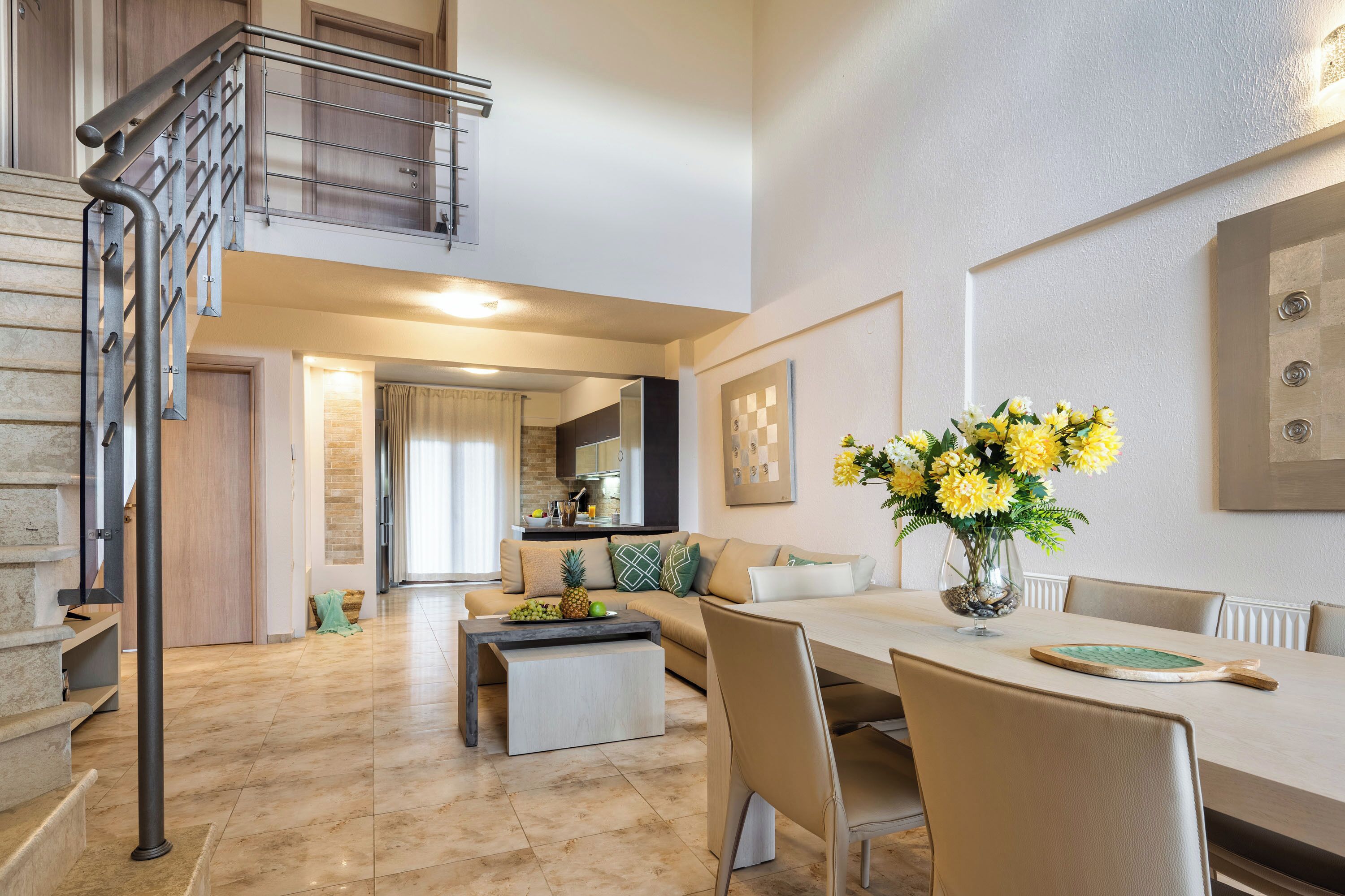Un espacio habitable amplio con una mesa de comedor, sillas y un sofá. Una escalera con barandilla metálica conduce a un nivel superior.